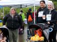 A family and baby in a stroller smile at the Gresham Lilac Run meeting zone.