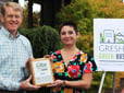 Two employees hold up a Green Business sign, after being designated as a Green Business. 