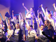 Group of singers on stage with the arms in the air performing the musical "Matilda".