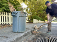 Man raking tree debris away from a storm drain to add to yard debris bin. 