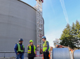 Three employees review plans, standing in front of a newly constructed water reservoir. 