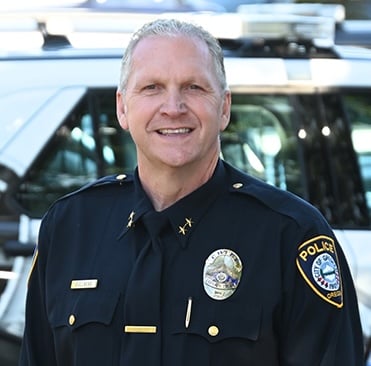 Chief Travis Gullberg in front of police cruiser. 