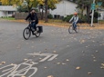 Two bicyclists ride on a Gresham Greenway bicycle route. They use a bicycle pavement marking in the street and a Greenway sign to find their way. 