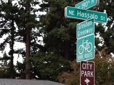 A green rectangular bike route sign and green rectangular Gresham Greenway sign mark the bicycle route near a city park. 