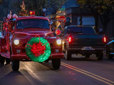 A vintage red fire truck with holiday lights carries Santa Claus down Main Avenue in historic downtown Gresham.