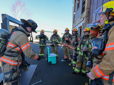 Fire recruits watch as an academy instructor demonstrates forcing a door.