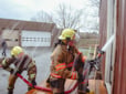 Spray from a fire hose rains down on recruits as they hose down a practice house.