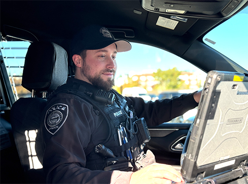 Officer sitting in patrol car, looking at computer.