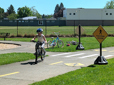 Child riding a bike by a Pedestrian Crossing sign.